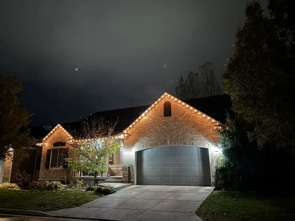 Brick rambler with warm white lights tracing the garage gable